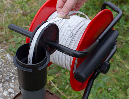 solinst well casing and depth indicator being used in field to take a reading from laser marked flat tape